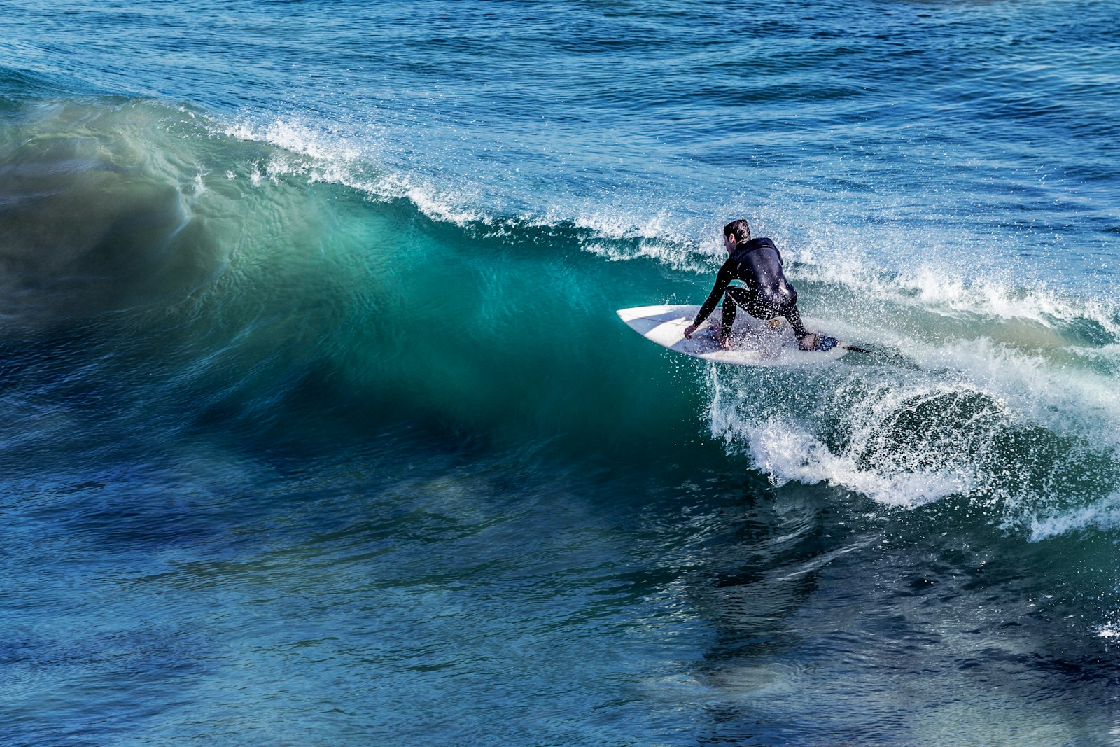 Surfer in a wetsuit carving down the face of a glassy green wave