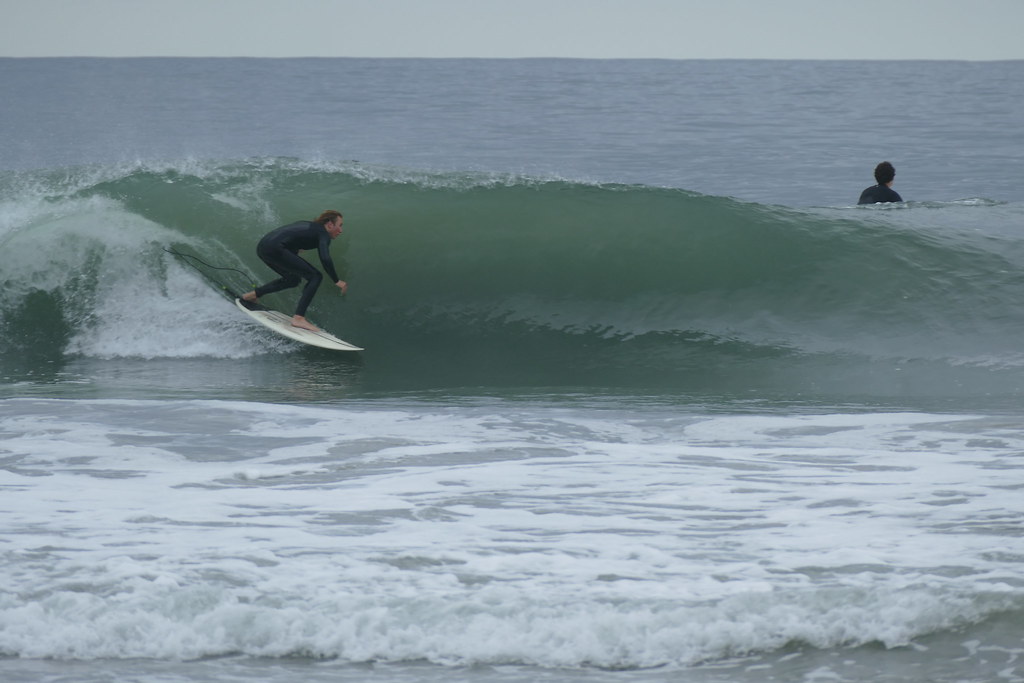 CdM surfer dropping in on a clean green wave while a teammate paddles out